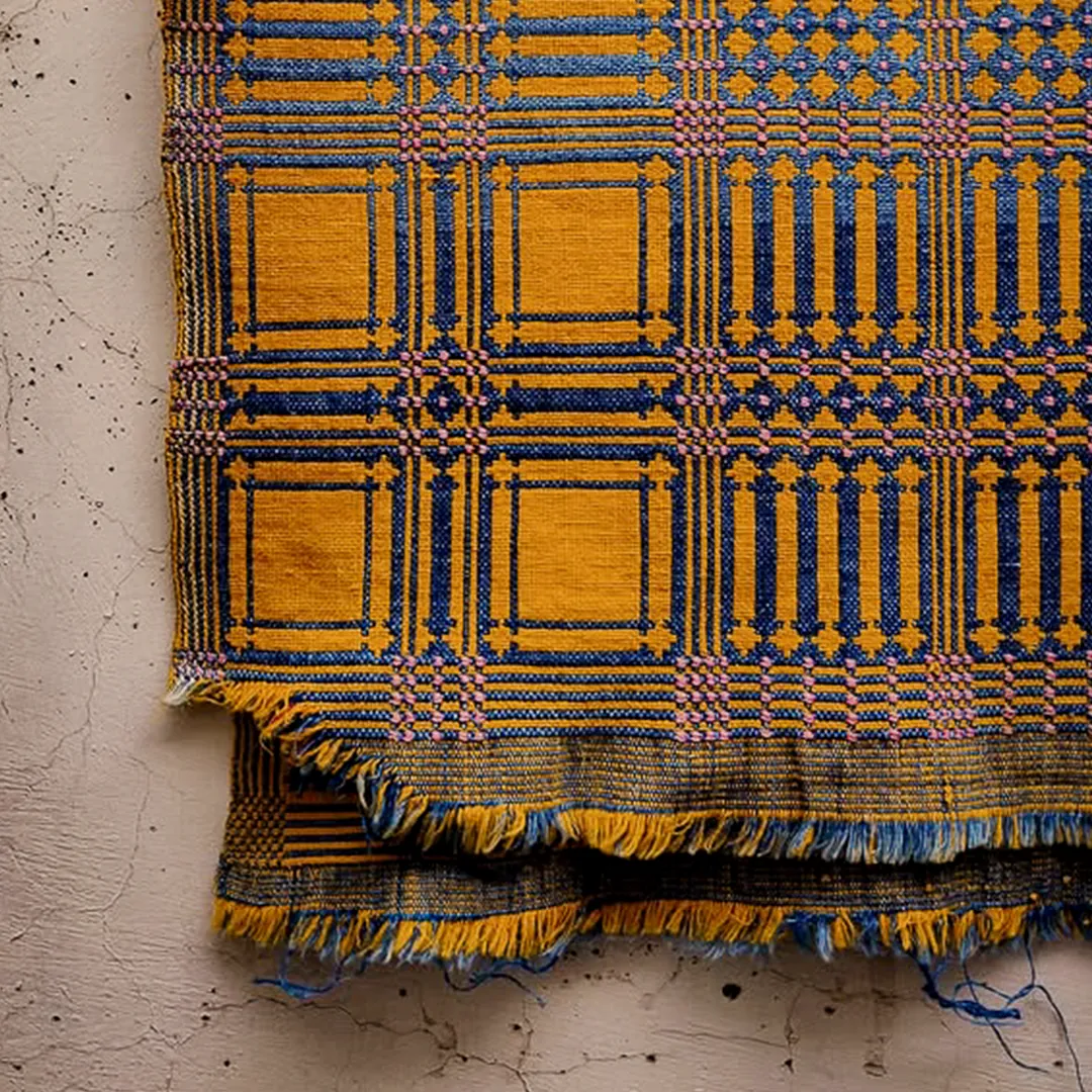 A handwoven khes, indigo and gold, fringed at the edge