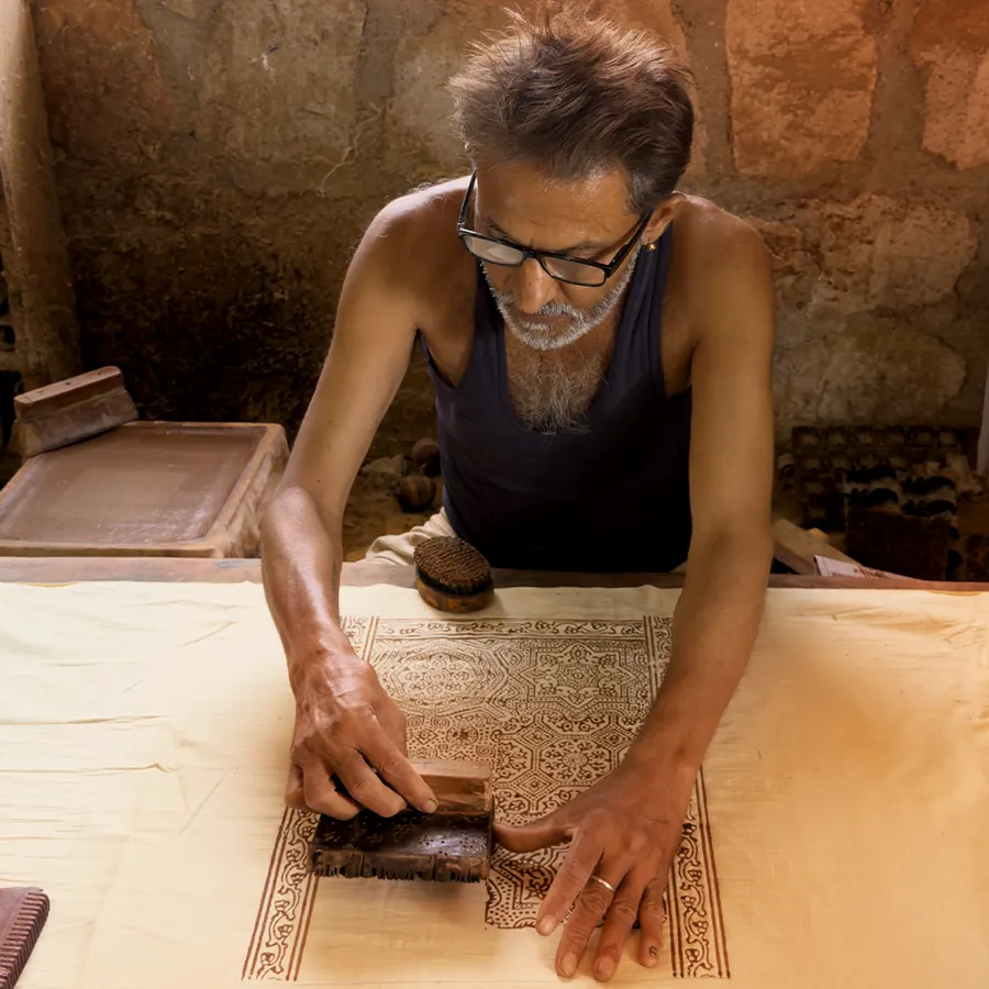A Khatri printer pressing a carved wooden block into cloth by hand