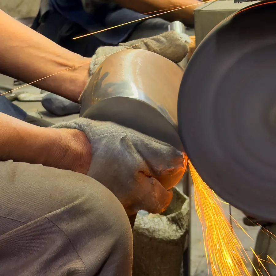 Two pairs of hands holding a curved iron piece to a grinding wheel, sparks flying